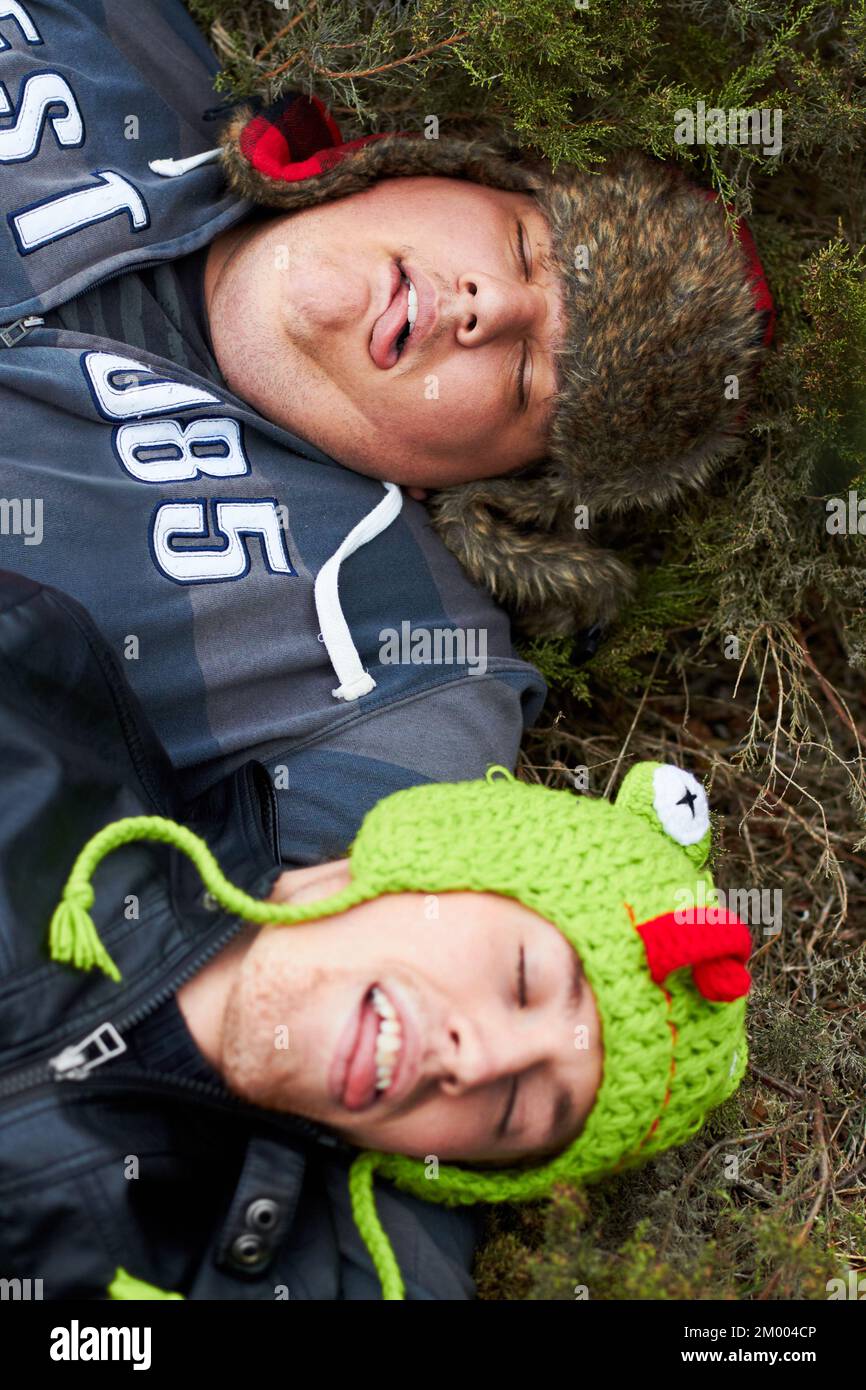 All partied out. An overweight man and his buddy lying passed-out on the grass with their tongues sticking out. Stock Photo