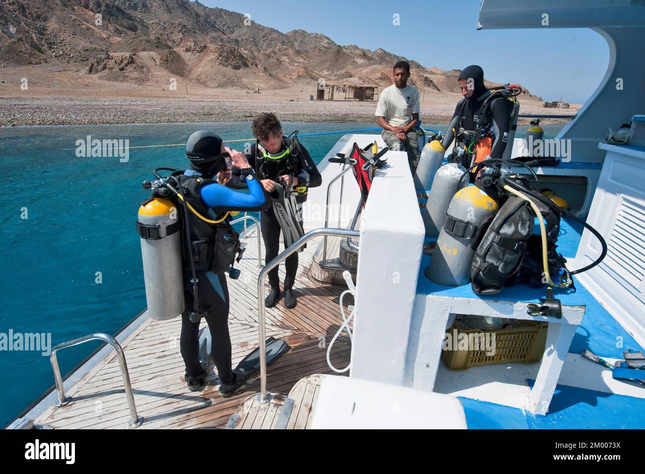 Divers standing on diving platform at the stern of diving boat preparing for dive, in the background rocky coast of Sinai Peninsula, Red Sea, Gabr el Stock Photo