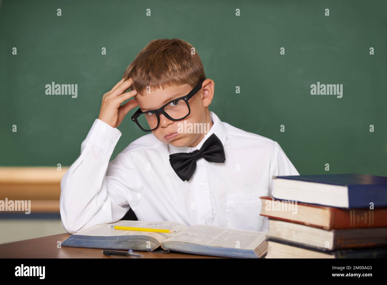 Not another pop-quiz. A young schoolboy in glasses and a bow-tie sighing wearily while looking at the camera. Stock Photo