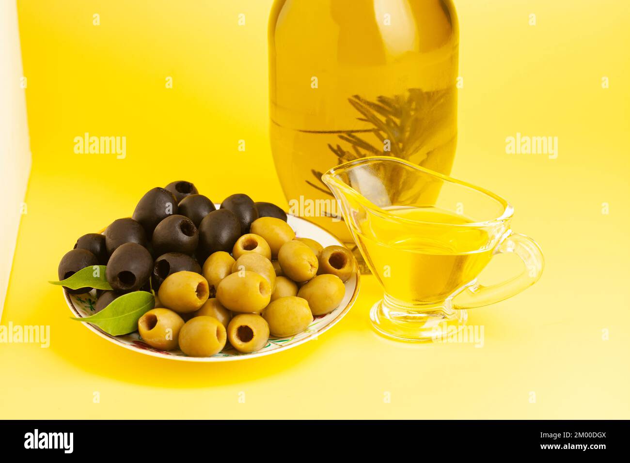 Jug with olive oil, green and black olives on yellow background Stock Photo
