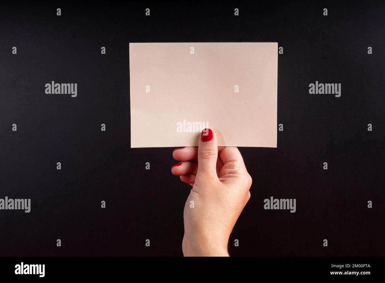 a5 postcard in horizontal format, held by a female hand on a black background with copy space and mockup Stock Photo