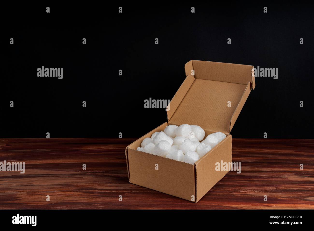 Styrofoam packing peanuts in cardboard box on dark wood background. White no plastic foam pellets protective for parcel packing. Stock Photo