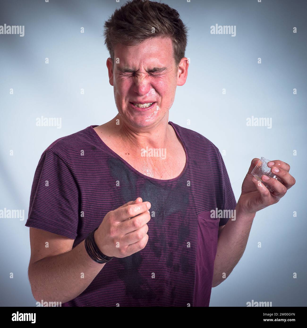 Drunk man, alcohol and wet tshirt with a tequila shot, party and celebration event in grey studio background. Young male partying, beverage and drink Stock Photo