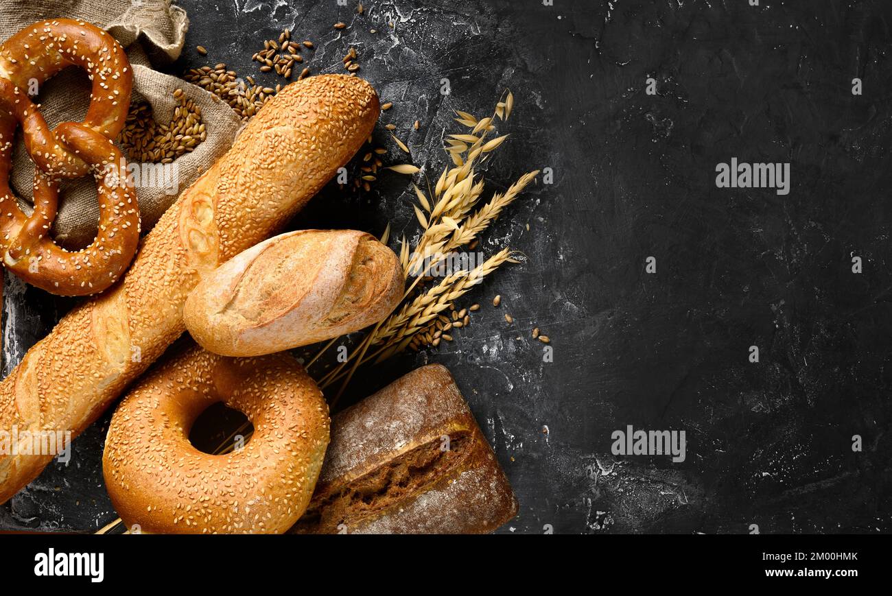 Fresh baked bread assortment on black textured board background. Top view Stock Photo