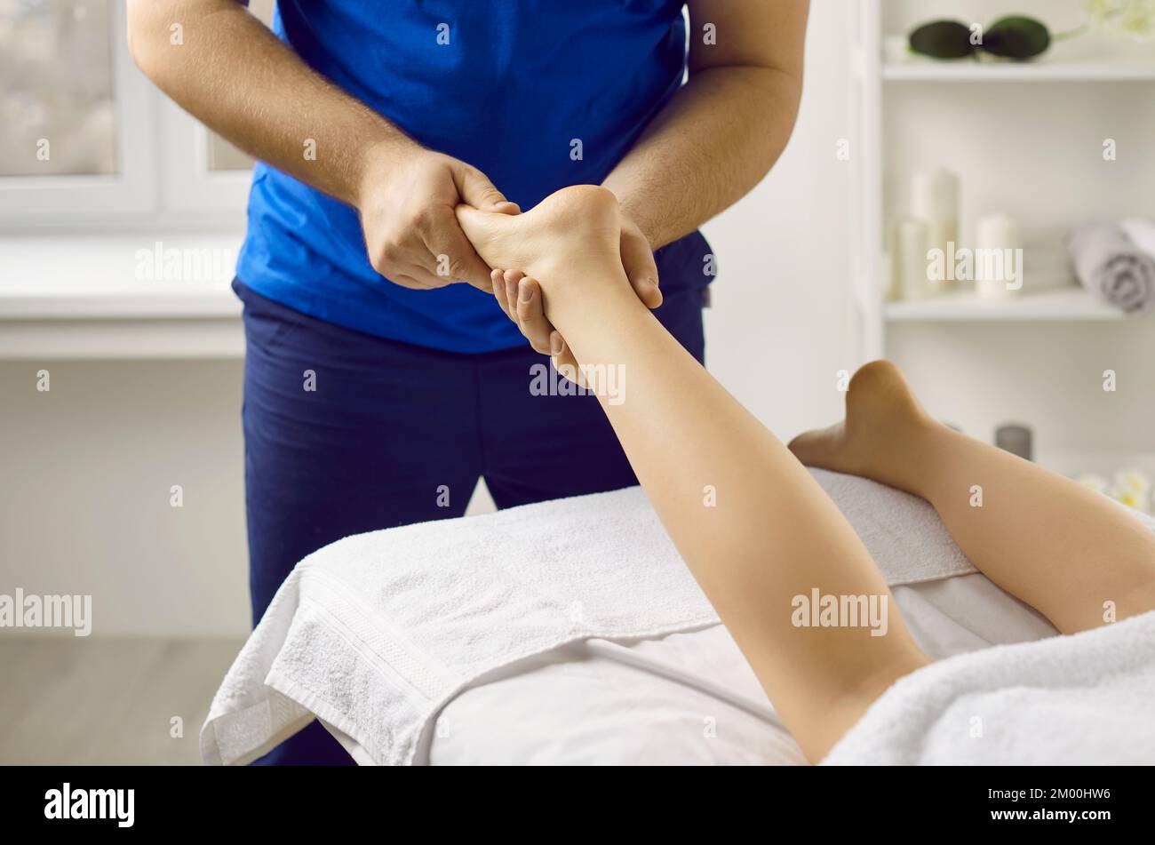 Male masseur in health clinic or massage parlor does hand massage of young woman's feet. Stock Photo