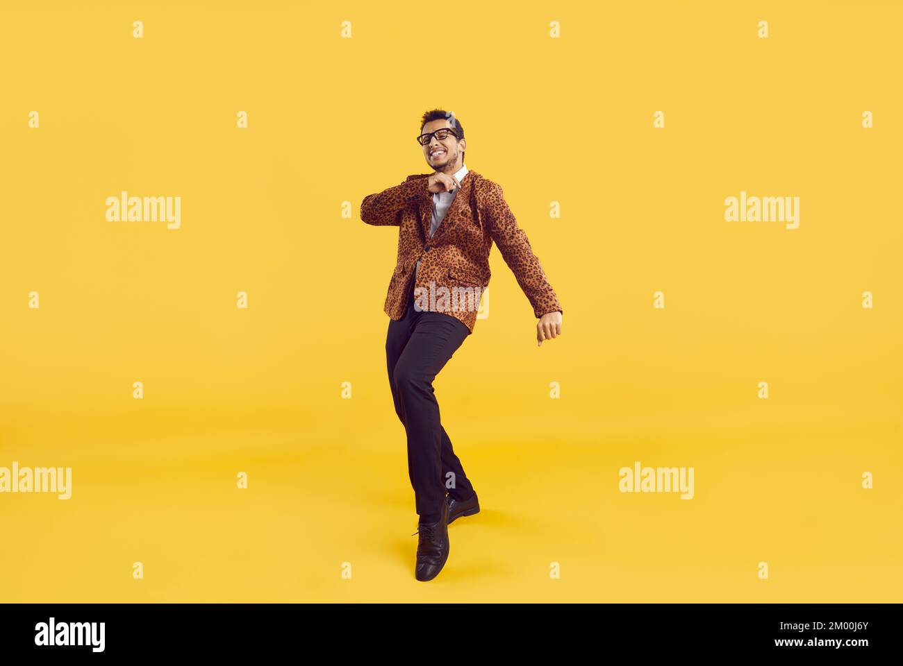 Funny young African American guy in a party jacket dancing on a yellow studio background Stock Photo