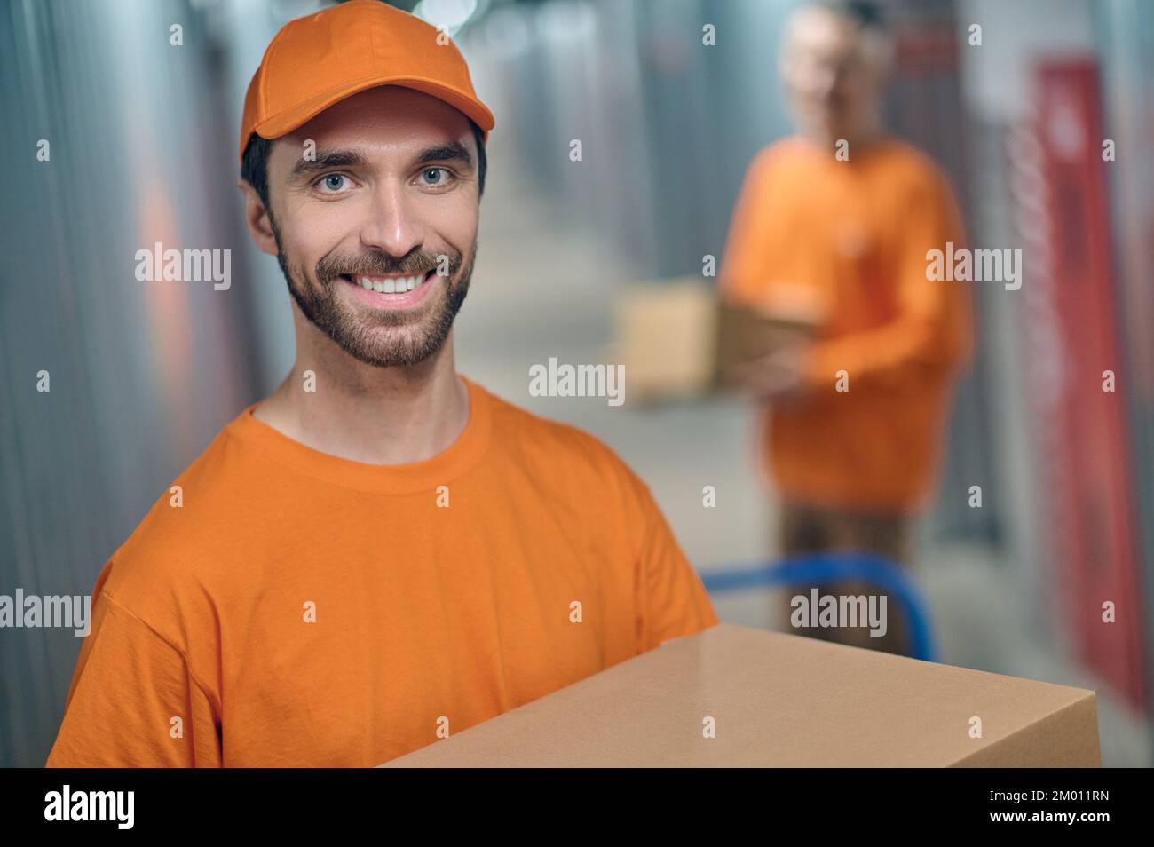 Smiling happy Caucasian male loader and his coworkers unloading boxed