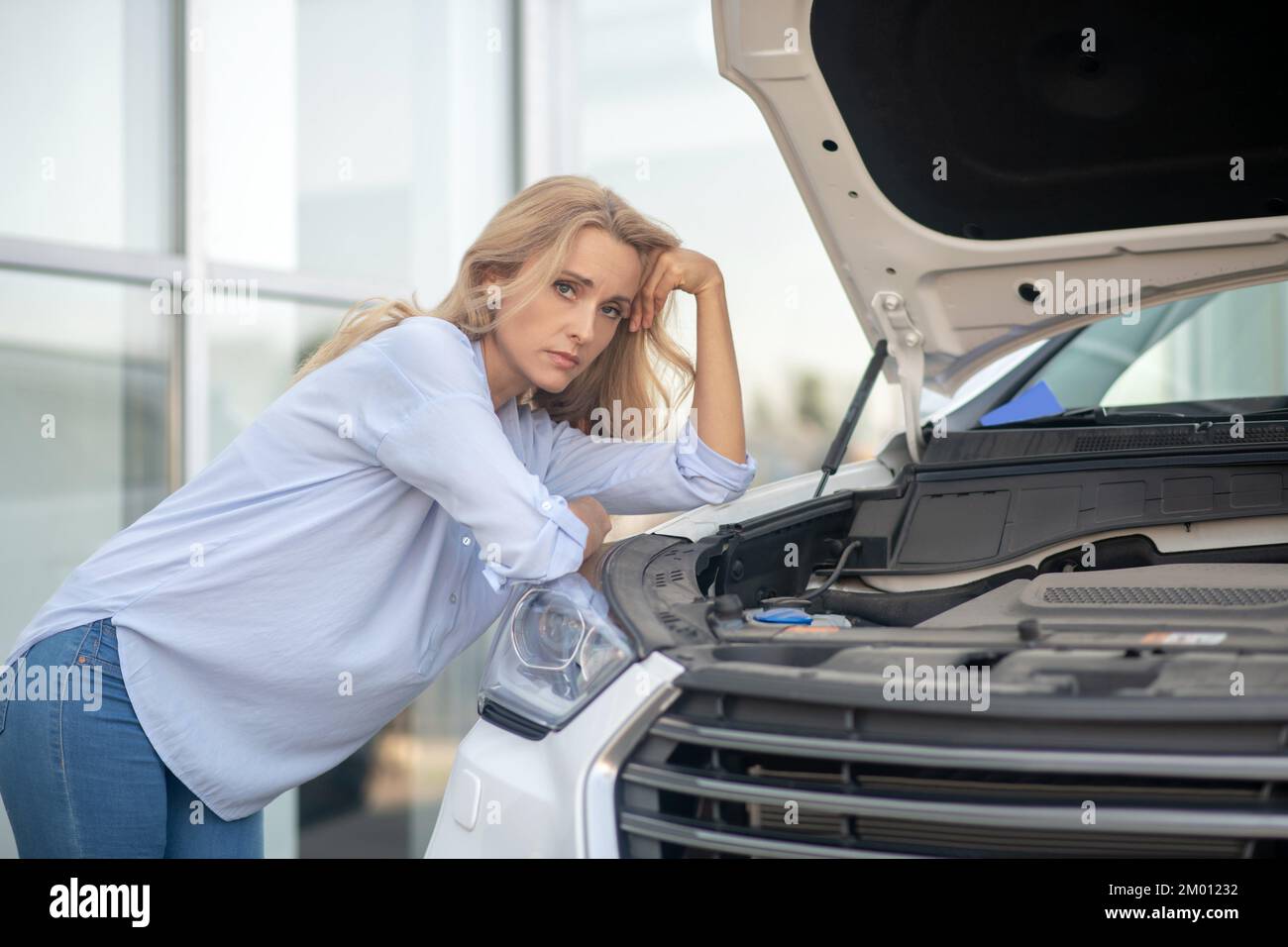 Car, problem. Blonde pretty woman standing sideways sad looking at