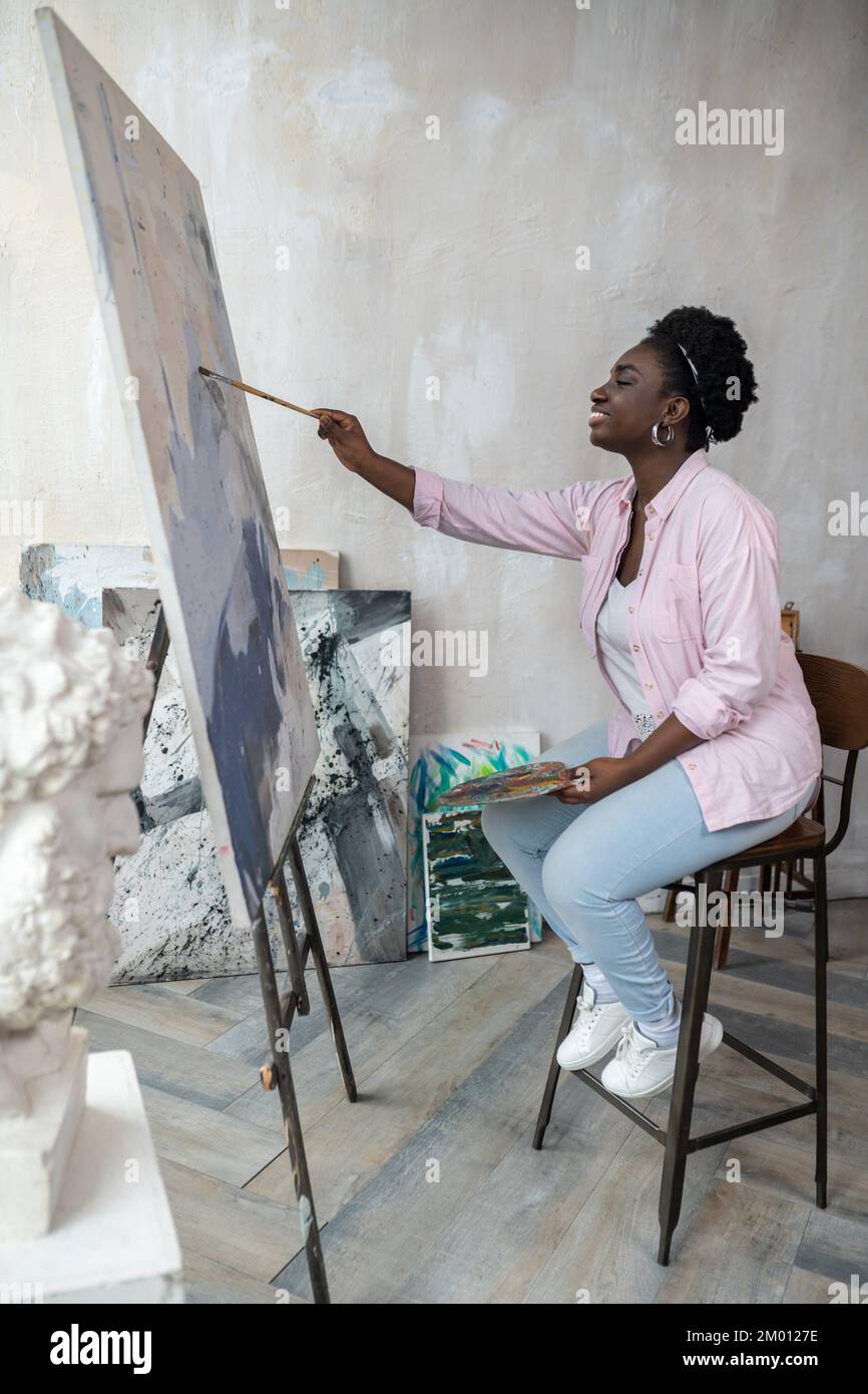 Artistry. A dark-skinned woman sitting near the easel and painting Stock  Photo - Alamy