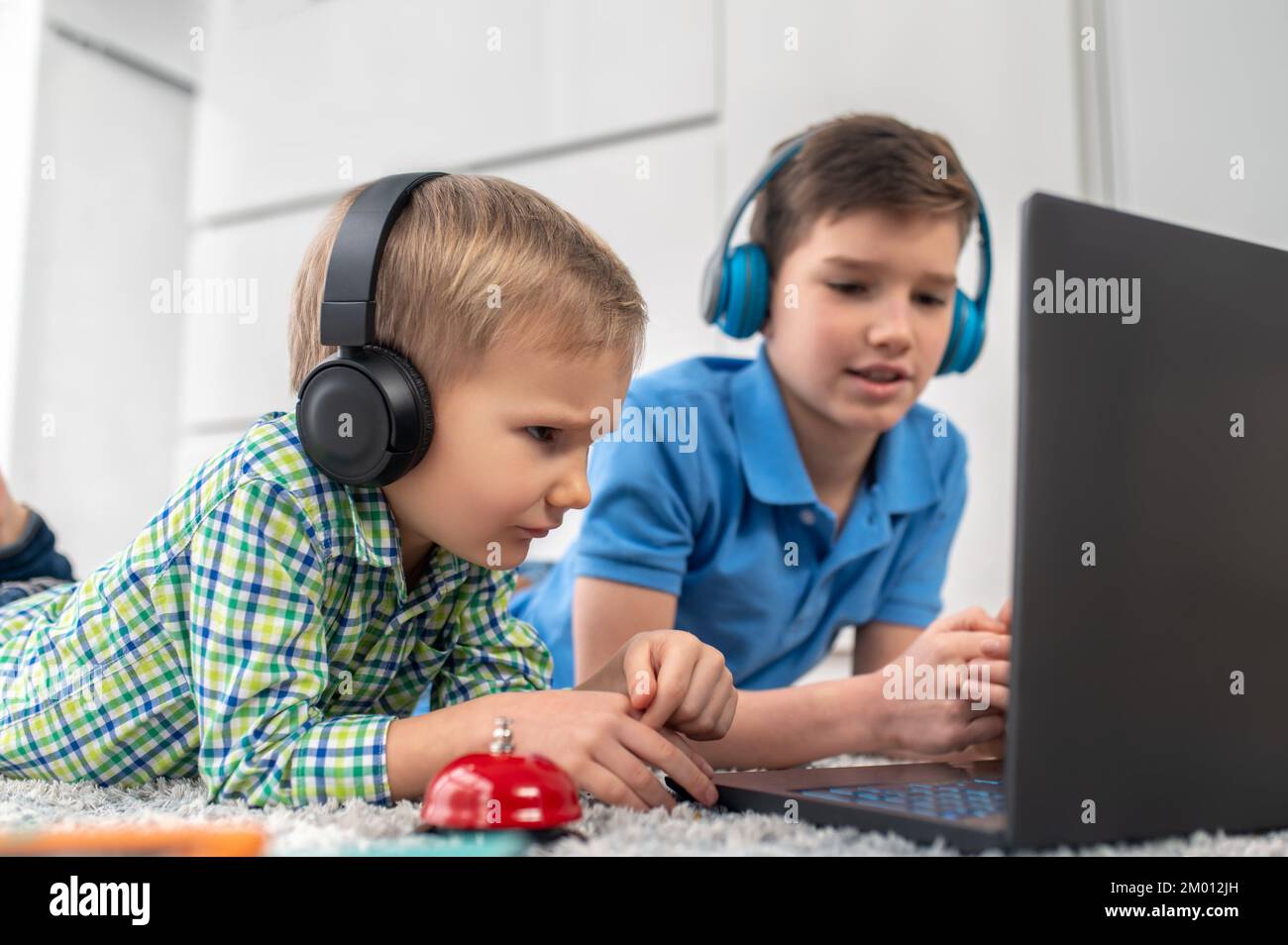 Focused child and his calm elder brother lying on the carpet before