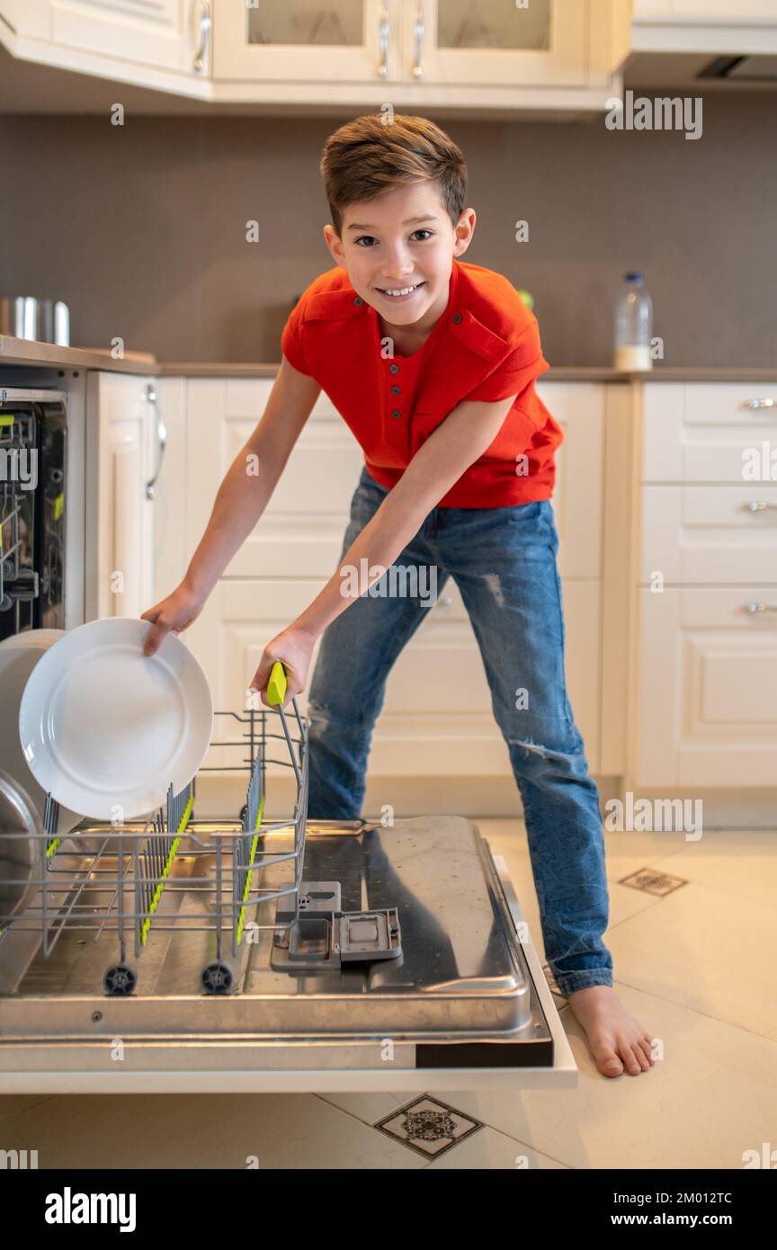 Fulllength portrait of a cheerful boy putting a dirty plate into an