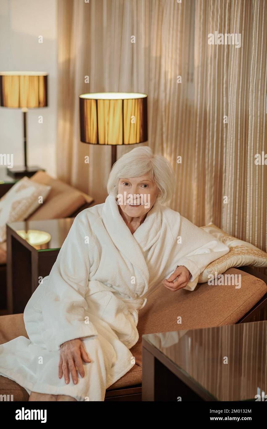 Morning. A good-looking old lady in a white robe in a hotel room. Stock Photo