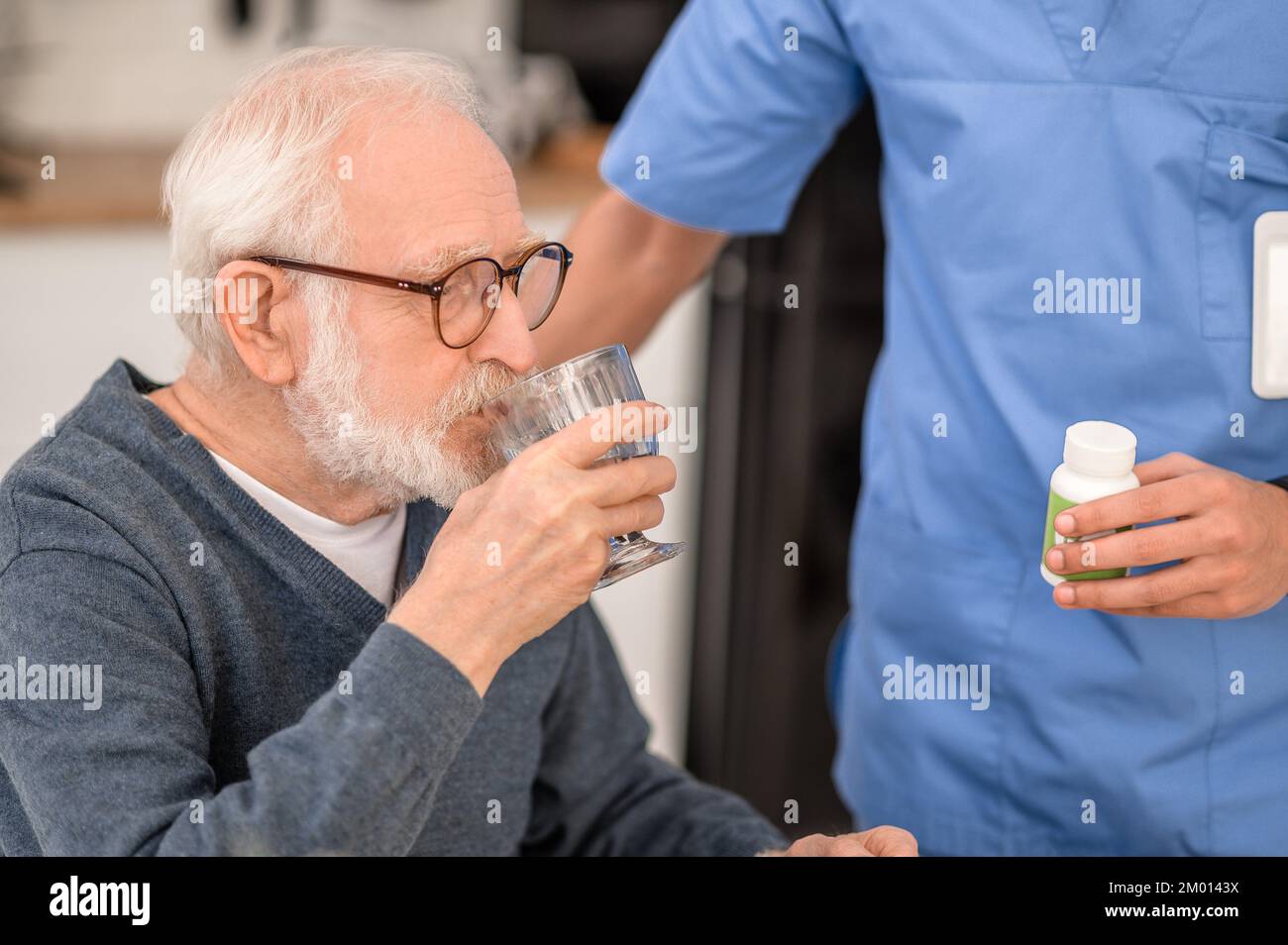 Elderly person washing down his pills with water under the supervision of his in-home nurse. Stock Photo