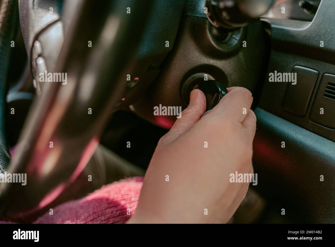 Closeup of a chauffeur seated at the car steering wheel turning the key in the ignition switch. Stock Photo