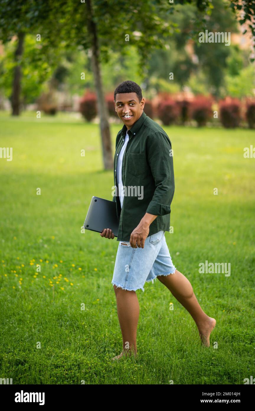 Close to nature. Darkskinned man walking barefoot on grass sideways to