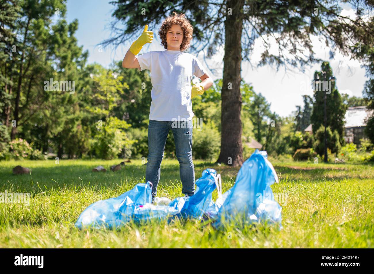 Good job. Confident teen standing near bags full with garbage Stock
