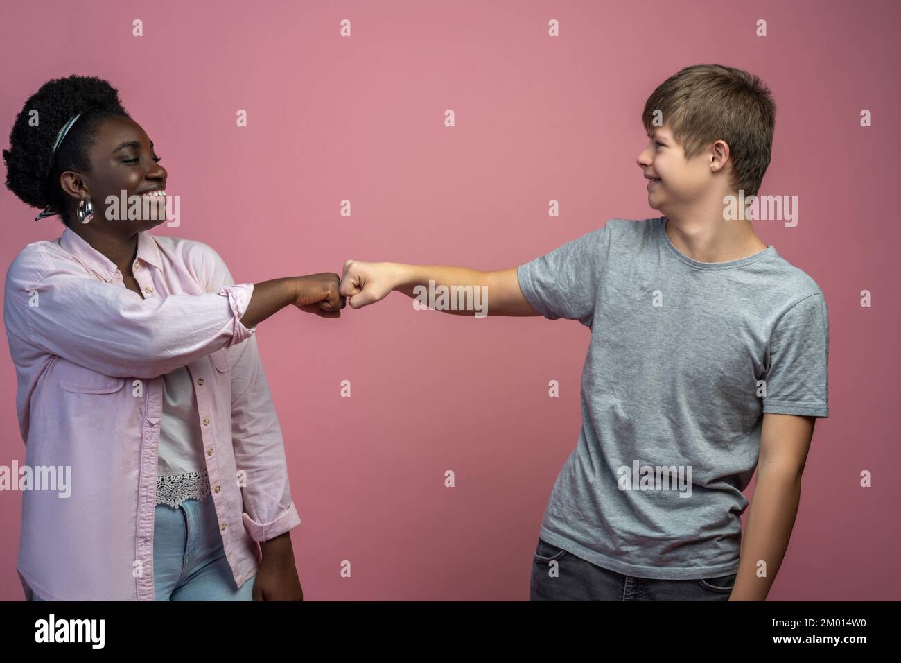 Understanding. Smiling guy with down syndrome and african american woman standing opposite touching with fist looking at each other. Stock Photo