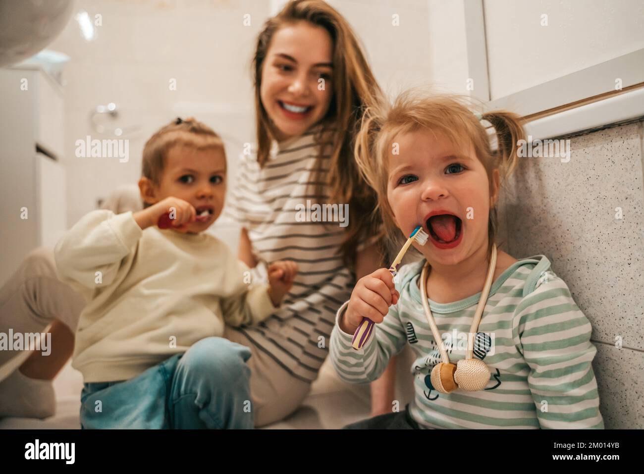 Cute little girls sitting on the bathroom floor and brushing the teeth