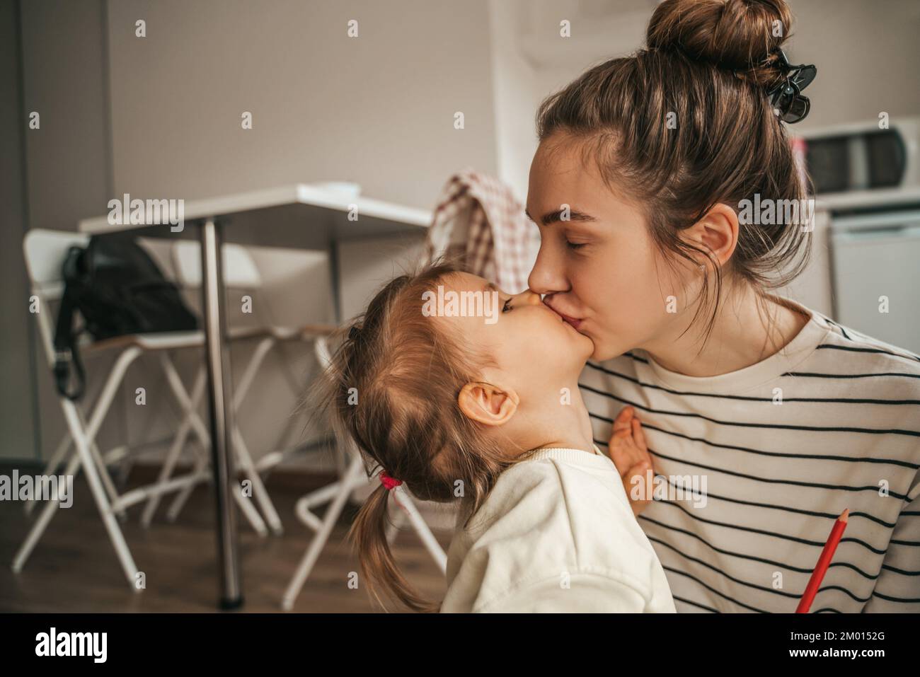 Loving beautiful young female parent giving a tender kiss to her child