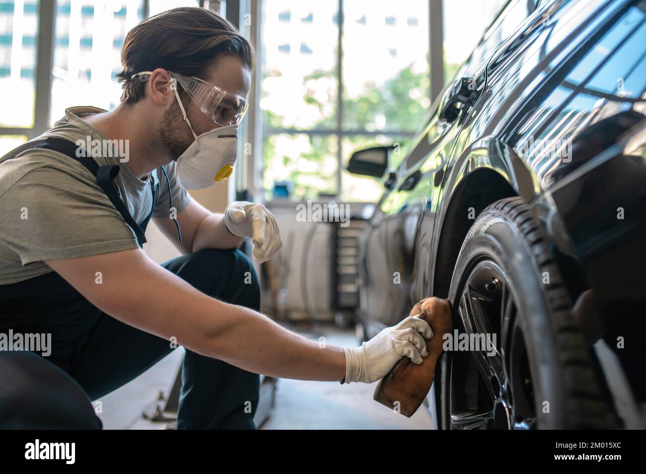 Professional car detailer in the automotive respirator buffing the