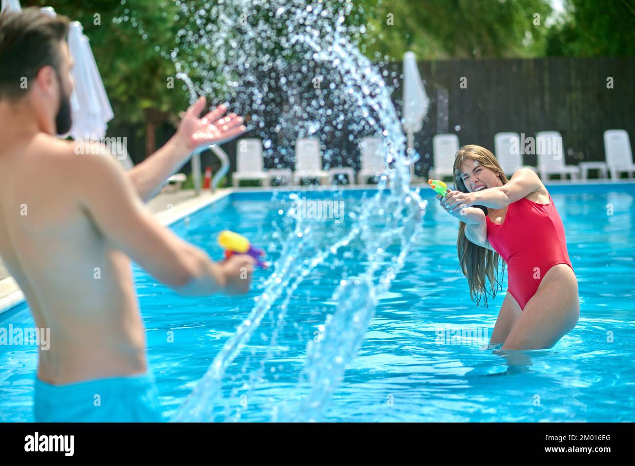 Woman And A Man Standing In The Swimming Pool And Shooting At Each Other With The Squirt Guns