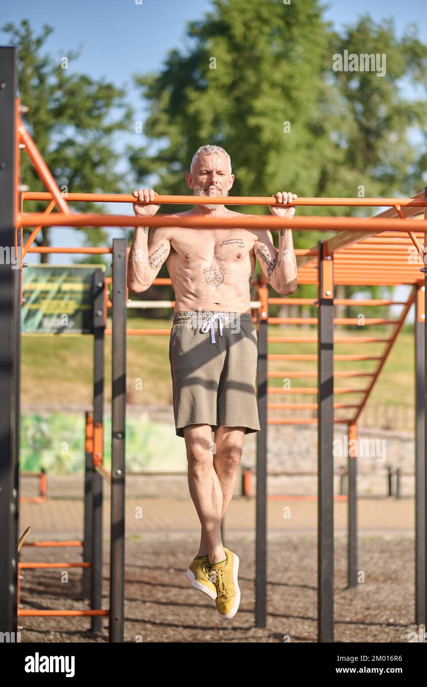 Sports ground. A gray-haired mature man having a workout on the open sports ground. Stock Photo