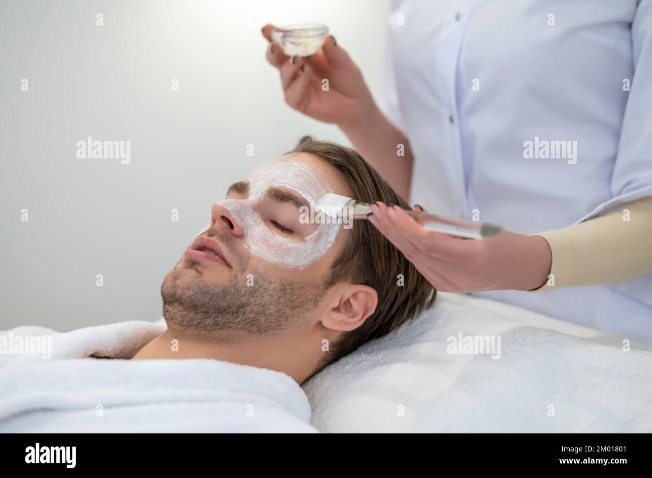 Facial mask. Beautician putting moisturizing mask on the clients face. Stock Photo