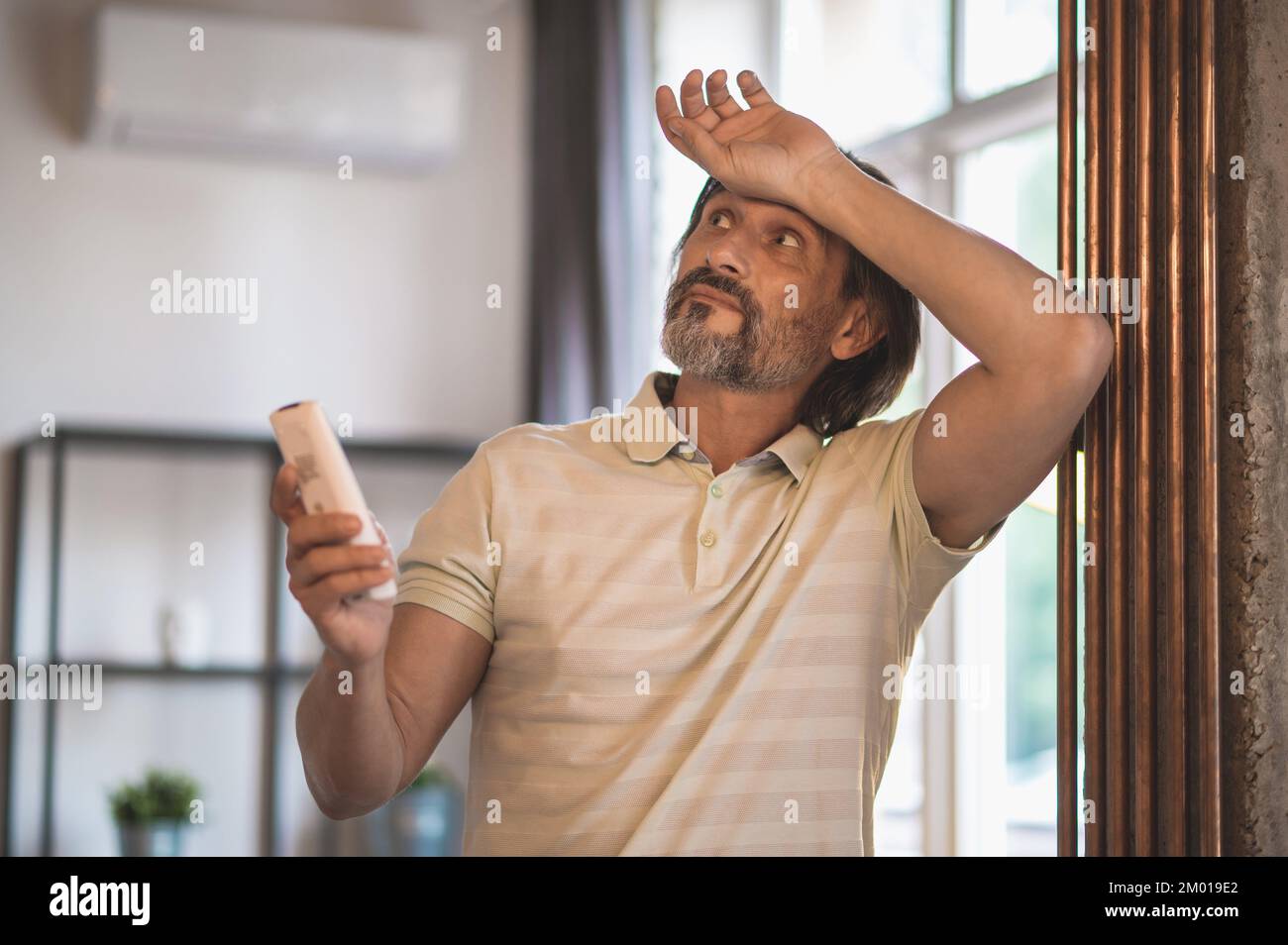 Heat. Man in white tshirt switching on the airconditioner Stock Photo