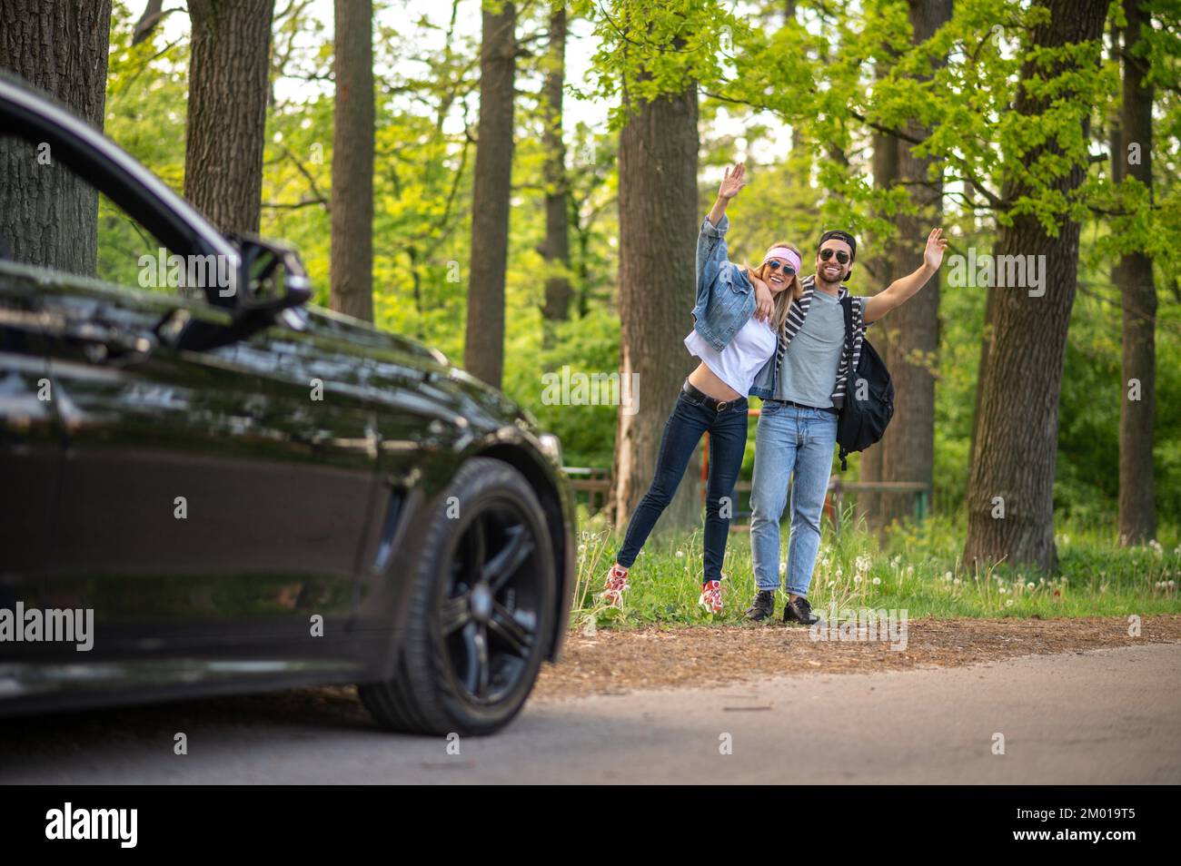 On the way to the city. Young people in the forest stopping the car and looking joyful. Stock Photo