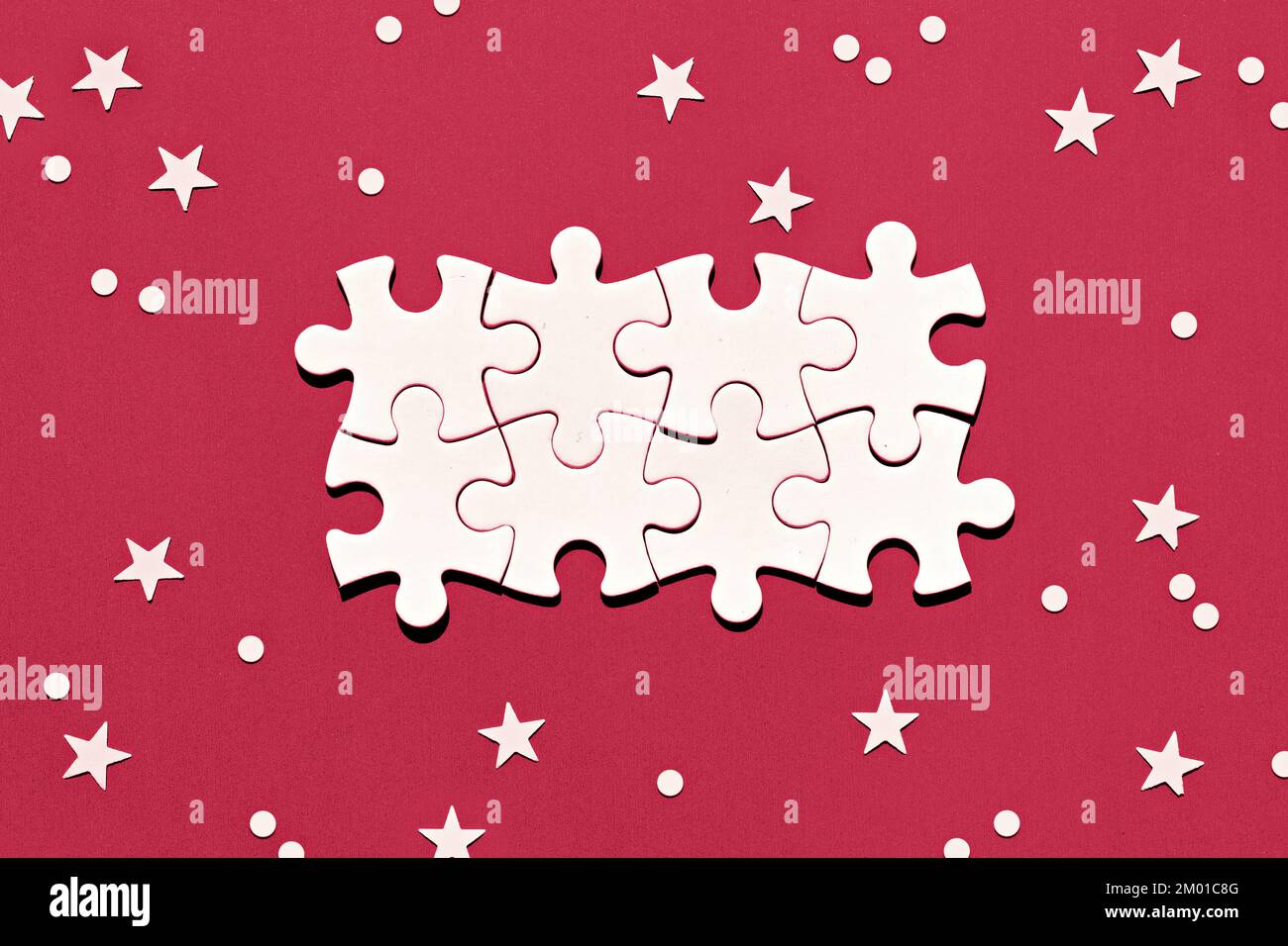 Puzzle pieces in the middle of red background toned in Viva Magenta color of the year 2023. Christmas background with snowflakes and stars. Christmas Stock Photo
