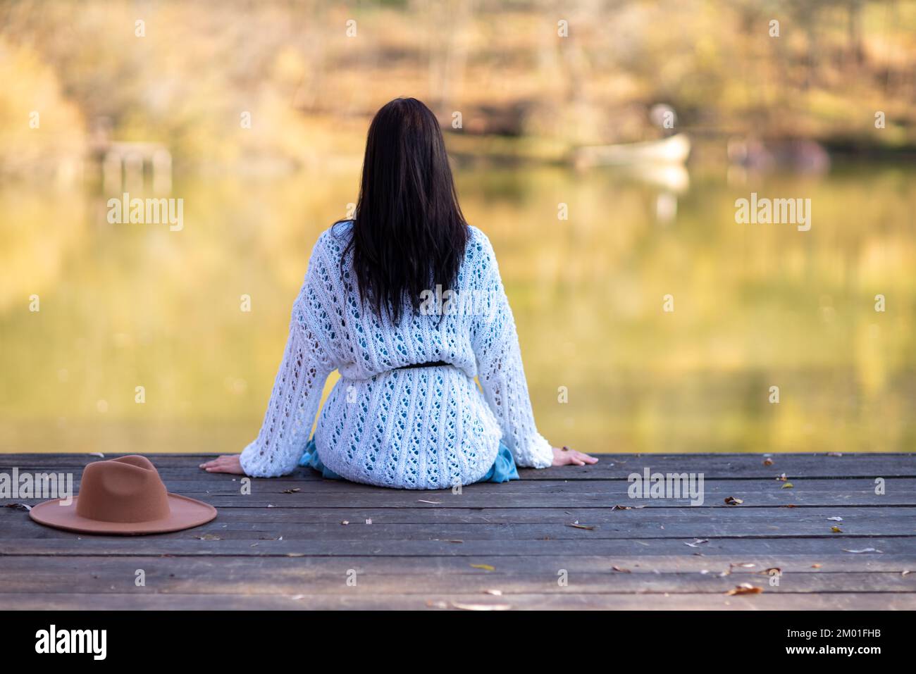 Autumn lake woman. She sits by a pond on a wooden pier in autumn and admires nature. The concept of tourism, weekends outside the city. Stock Photo