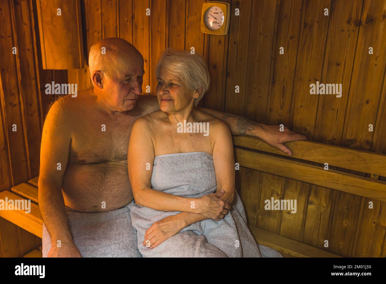 Caucasian married heterosexual senior couple sitting close to each other in wooden sauna. Spa and relaxation concept. High quality photo Stock Photo
