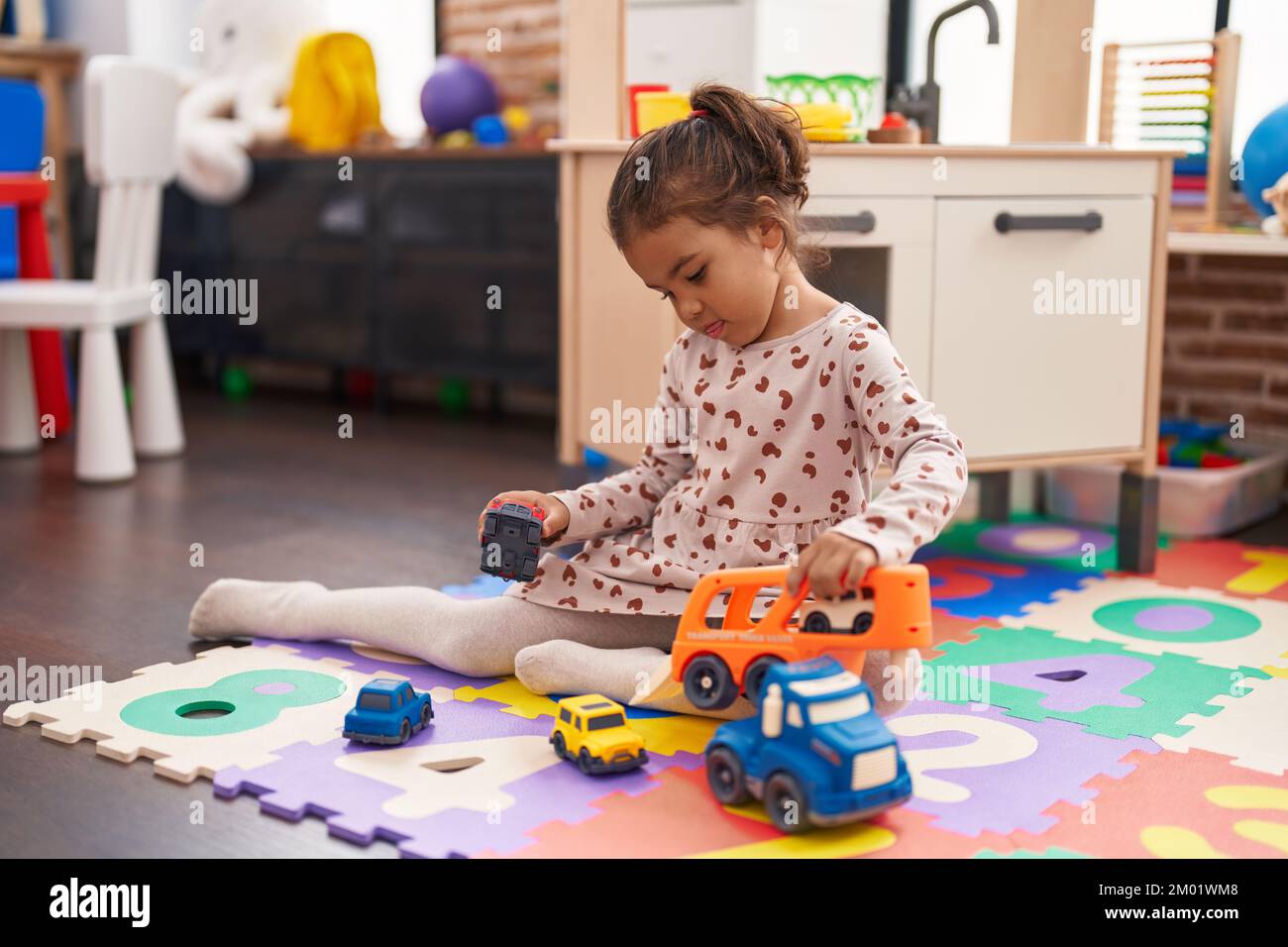 Adorable hispanic girl playing with car toy sitting on floor at ...