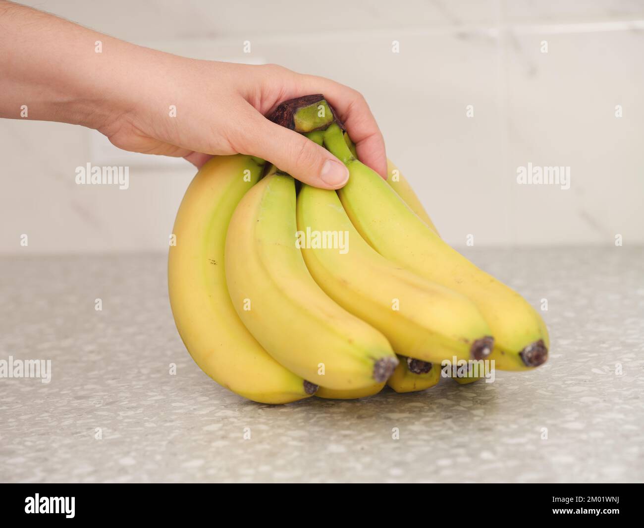 A woman picking up a bunch of bananas off of a counter top. Close up. Stock Photo