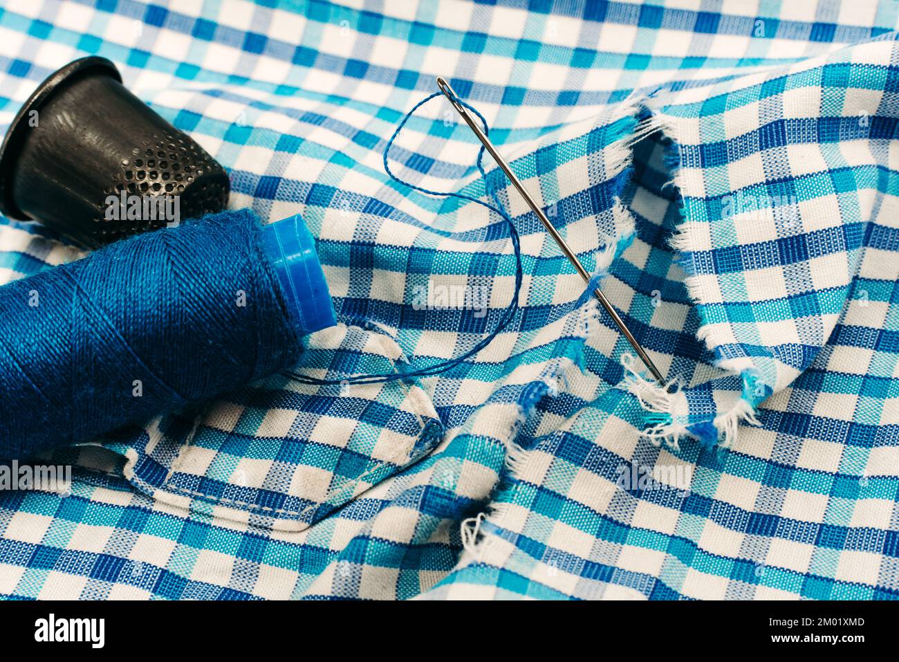 A needle and thread lies on torn or holey clothes. Shirt with a hole. Work for a seamstress or tailor Stock Photo