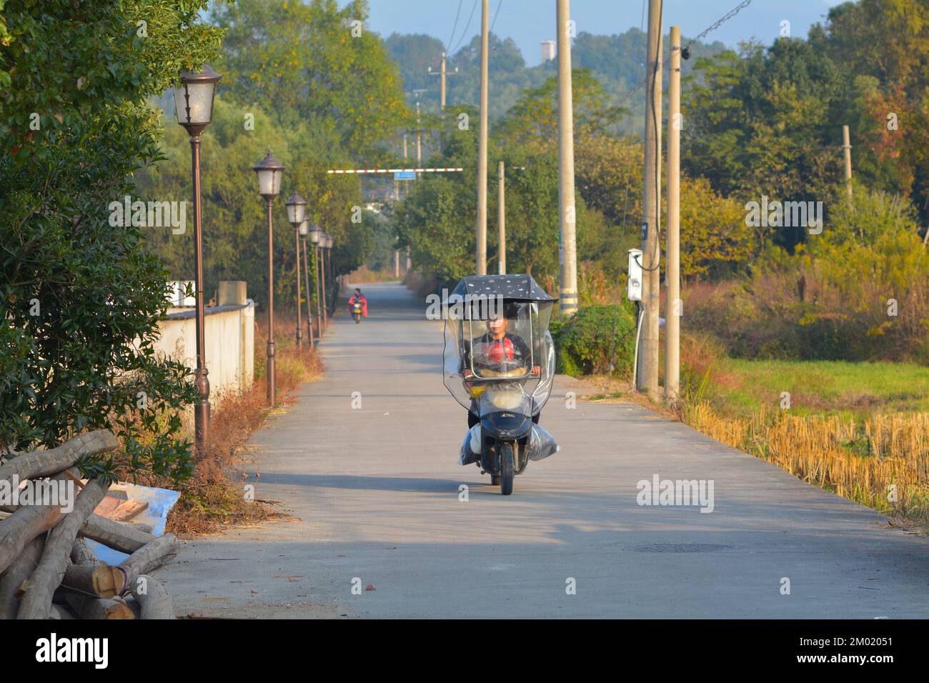 Street life in a small village in rural China. Moped drivers going through the quiet countryside. Stock Photo