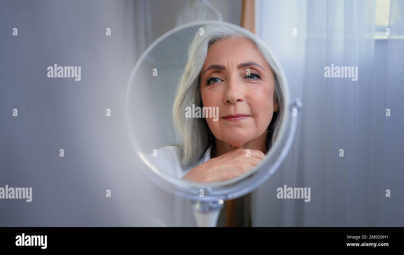Mirror reflection female wrinkled face 50s middle-aged Caucasian woman senior lady looking self lover skin care grandmother thinking pampering Stock Photo