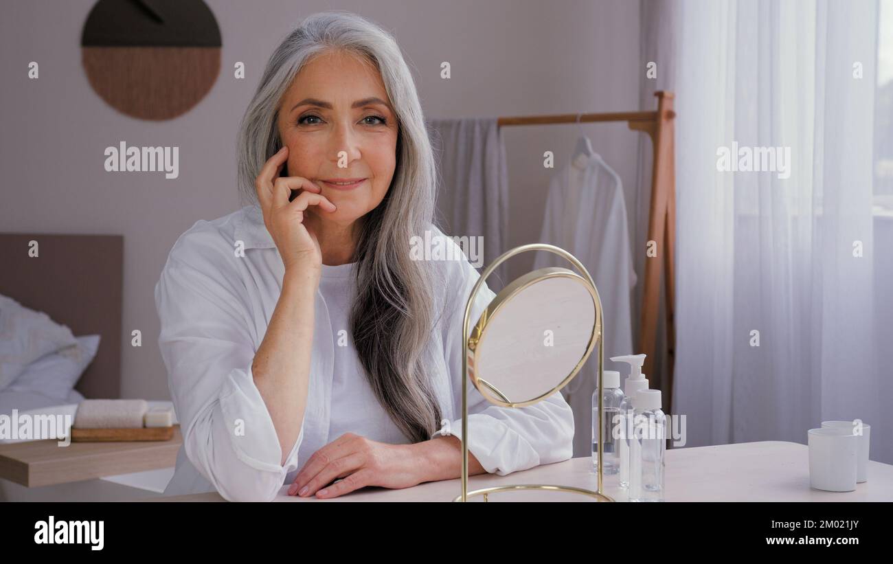 Caucasian old beautiful 60s senior lady mature aging elderly model woman with gray hair female granny grandmother looking at camera sitting at home Stock Photo