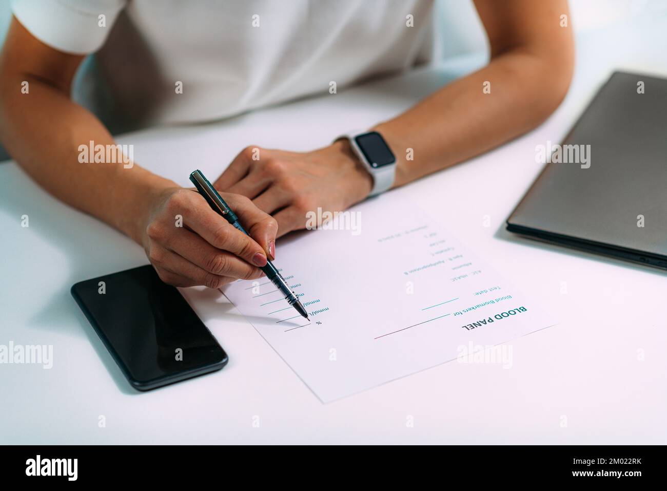 Woman writing down blood test results on a form using her smartphone. Stock Photo