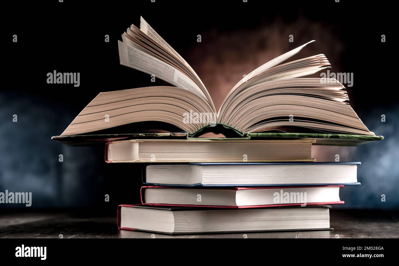 A composition with an open book lying on a stack of other books Stock Photo