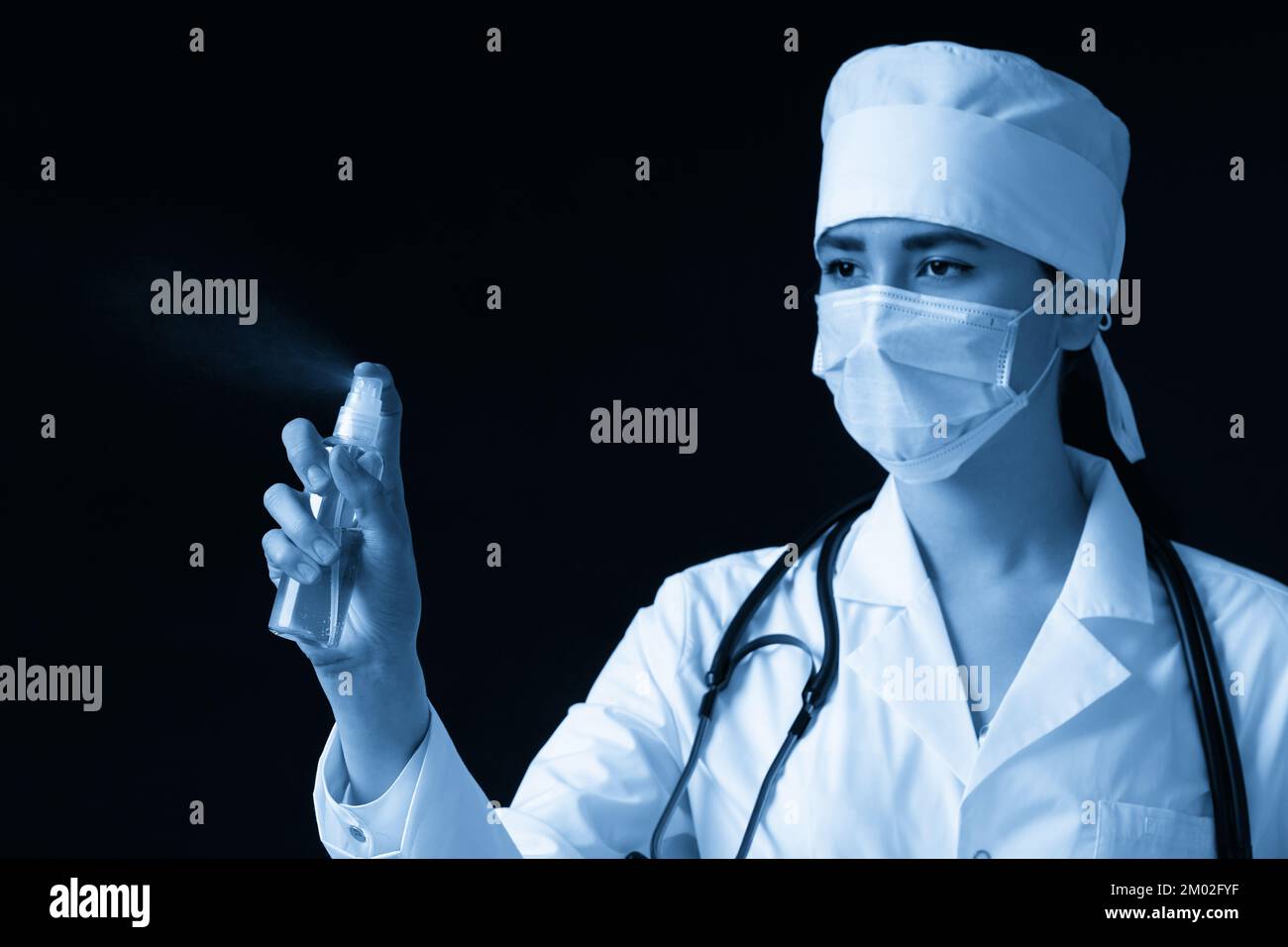 Young female doctor using spray antiseptic spray over black background ...