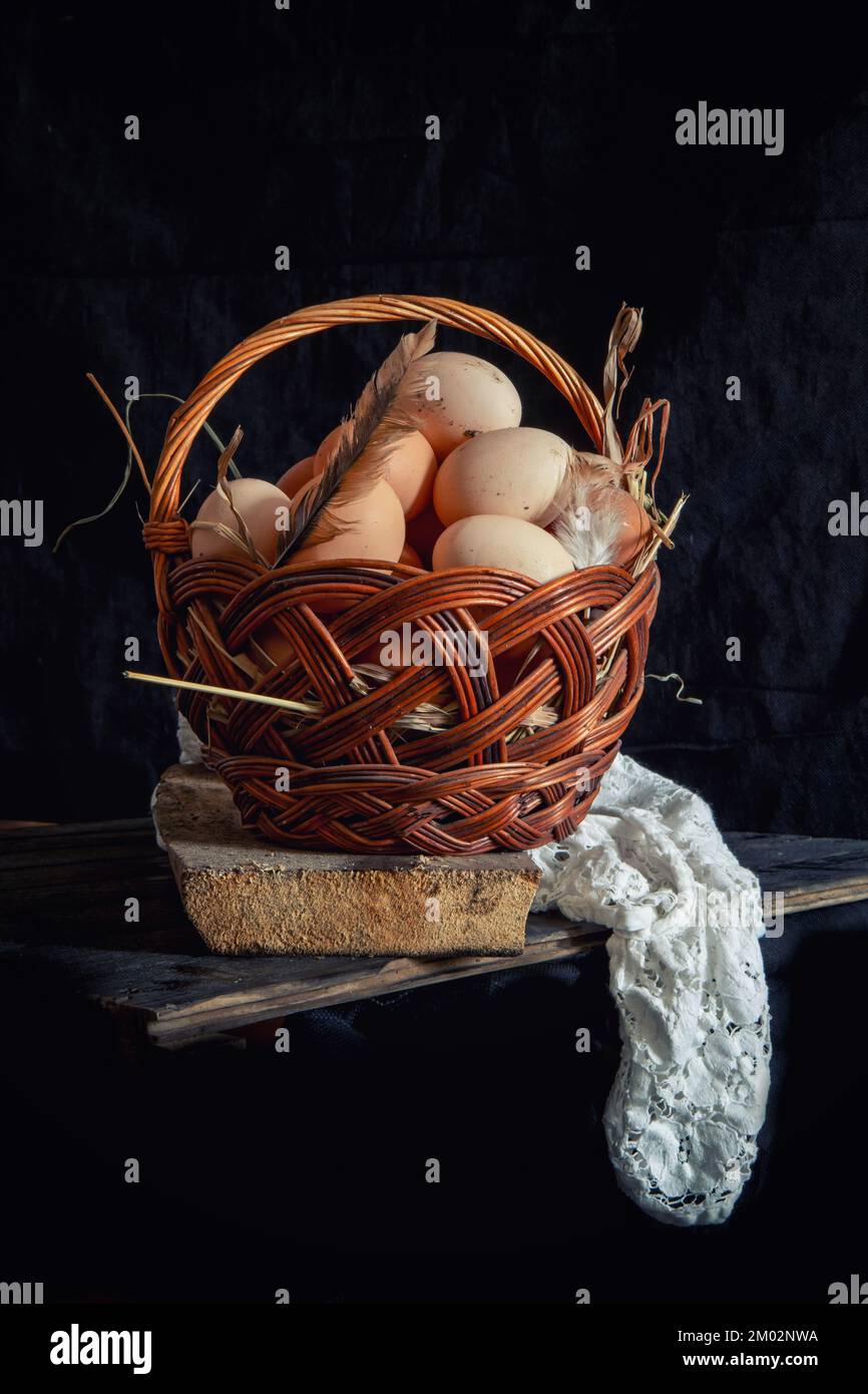 Chicken eggs in a wicker basket on a dark background. Stock Photo