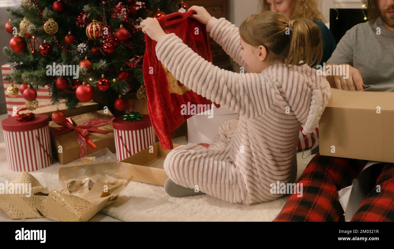 Happy caucasian family opening gifts on Christmas under decorated Christmas tree. They unpacking sweaters. Warm atmosphere at home on Christmas or New Year. Winter holidays. Santa Claus gifts. Stock Photo
