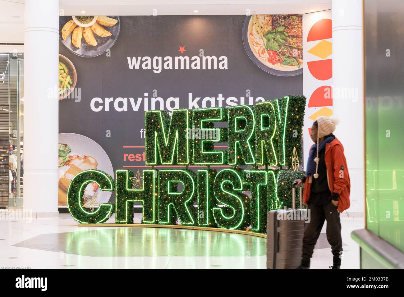 man with a shopping suitcase in a London shopping mall decorated with Merry Christmas tree and lights outside Wagamama restaurant England UK Stock Photo