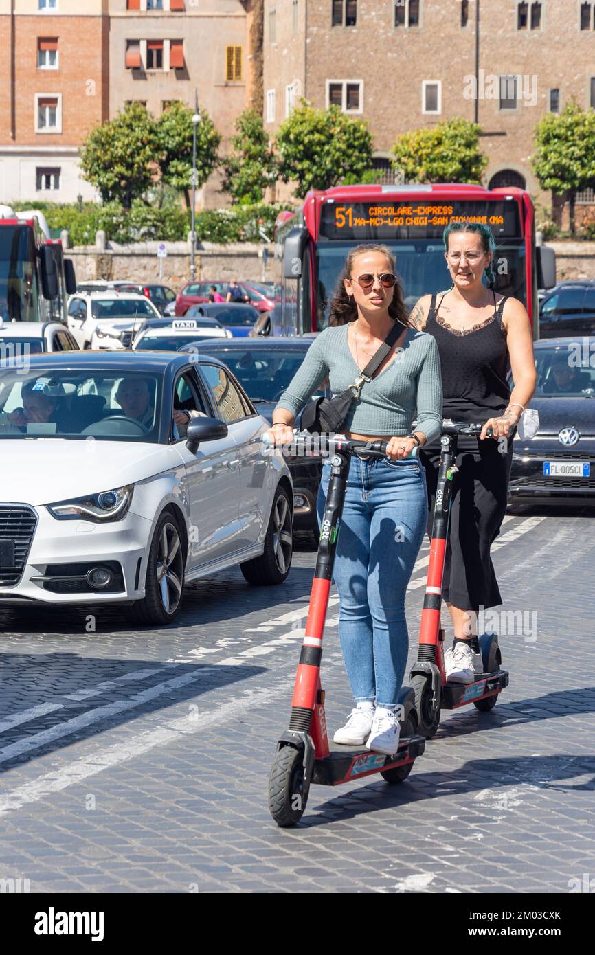 Women riding electric scooters on road, Piazza della Bocca della Verità, Forum Boarium, Ripa, Rome (Roma), Lazio Region, Italy Stock Photo