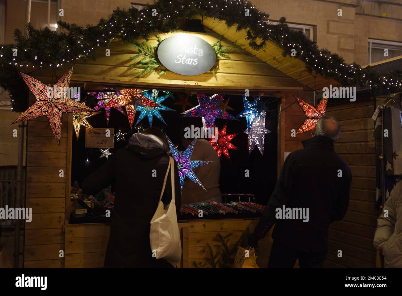 Christmas market stalls in Oxford, UK. Customers examine goods on sale. Stores stay open later hoping to increase sales over Christmas. Stock Photo