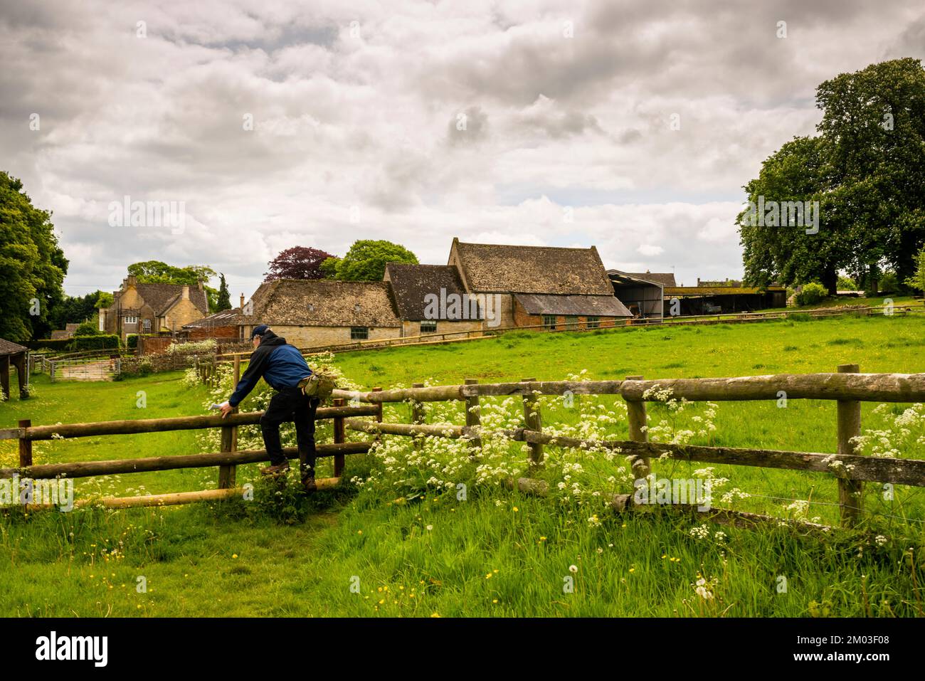 Step over fence and English farm buildings on the Cotswolds Way