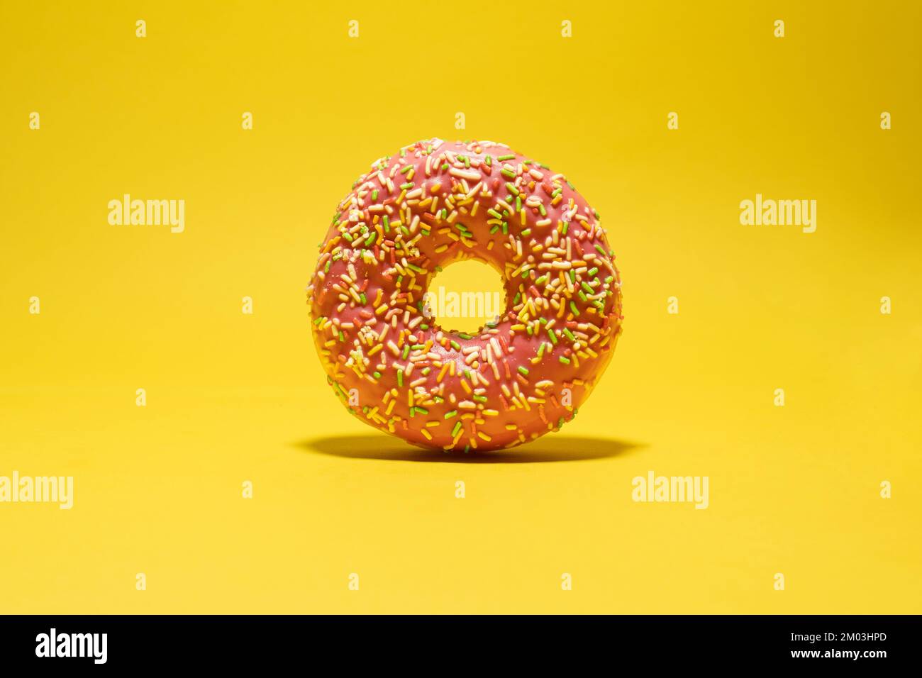 Pink donut with multicolored sprinkles on yellow background. Creative food background Stock Photo