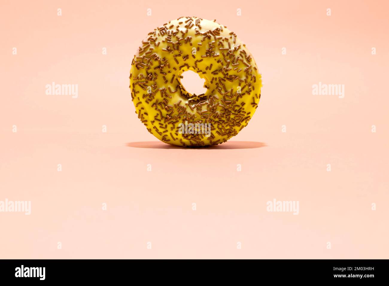 Yellow donut with chocolate crumbs on light pink background. Creative food background Stock Photo