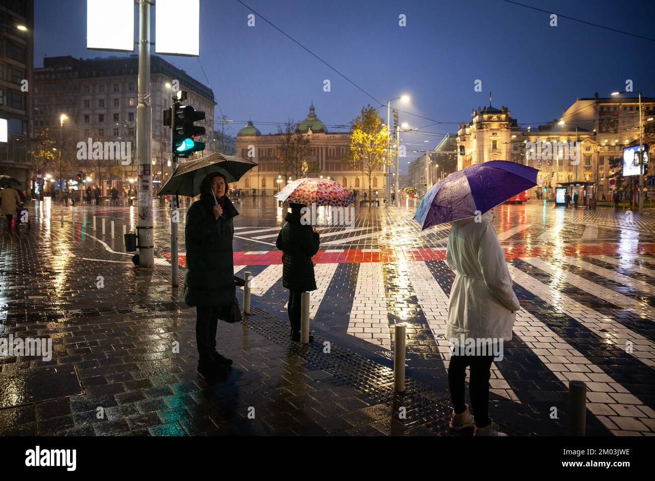Picture of people with an umbrella waiting for green light to cross a crossroad in the city center of Belgrade, during heavy rains, in autumn. Stock Photo